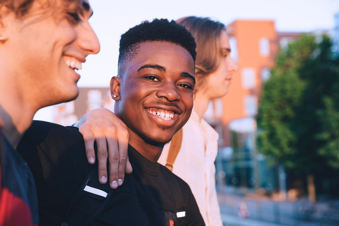 One teen smiles at the camera with two others beside him outside at sunset
