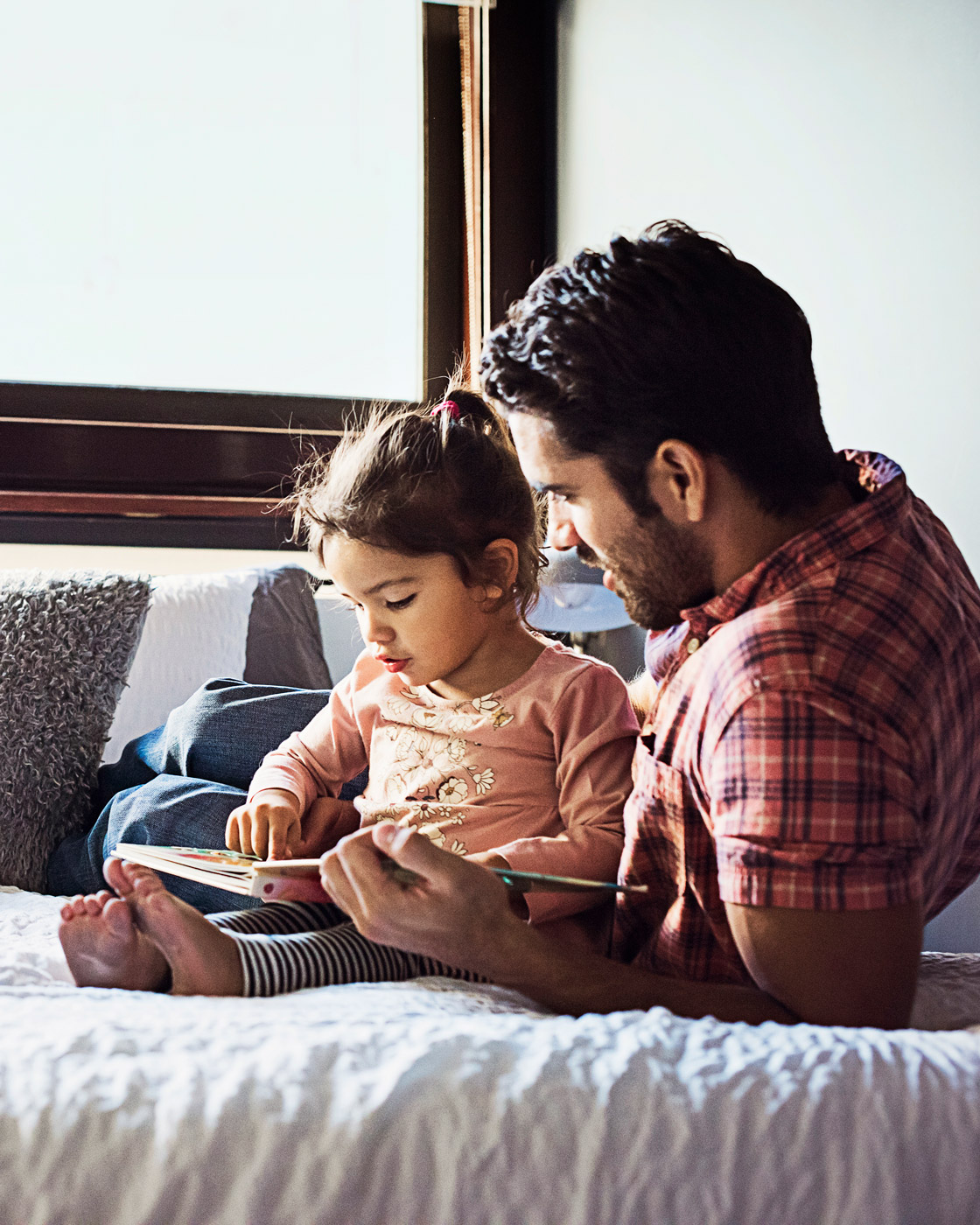 Father and daughter sitting on a bed reading a book together